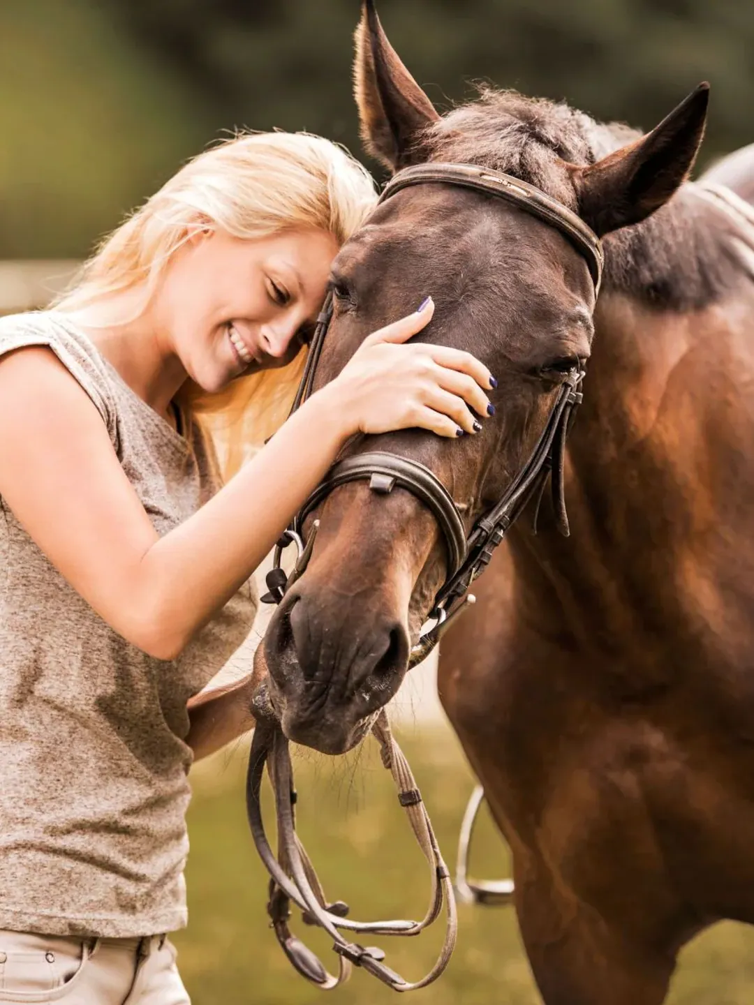 A photograph of a woman resting her forehead against her bay horse’s face, one hand on its cheek.