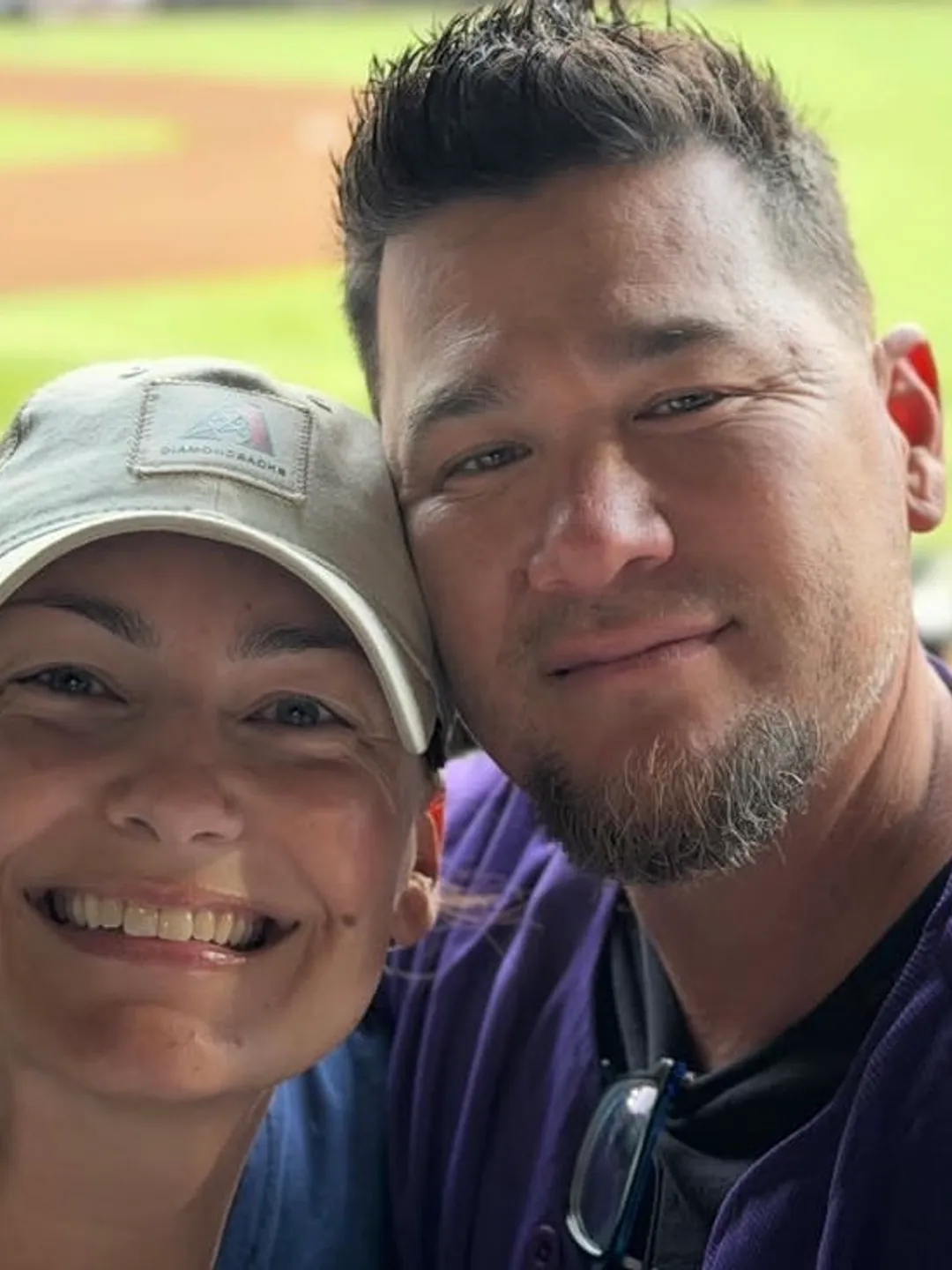 A photograph of a couple at a ball game, cheek to cheek, her cap still on.